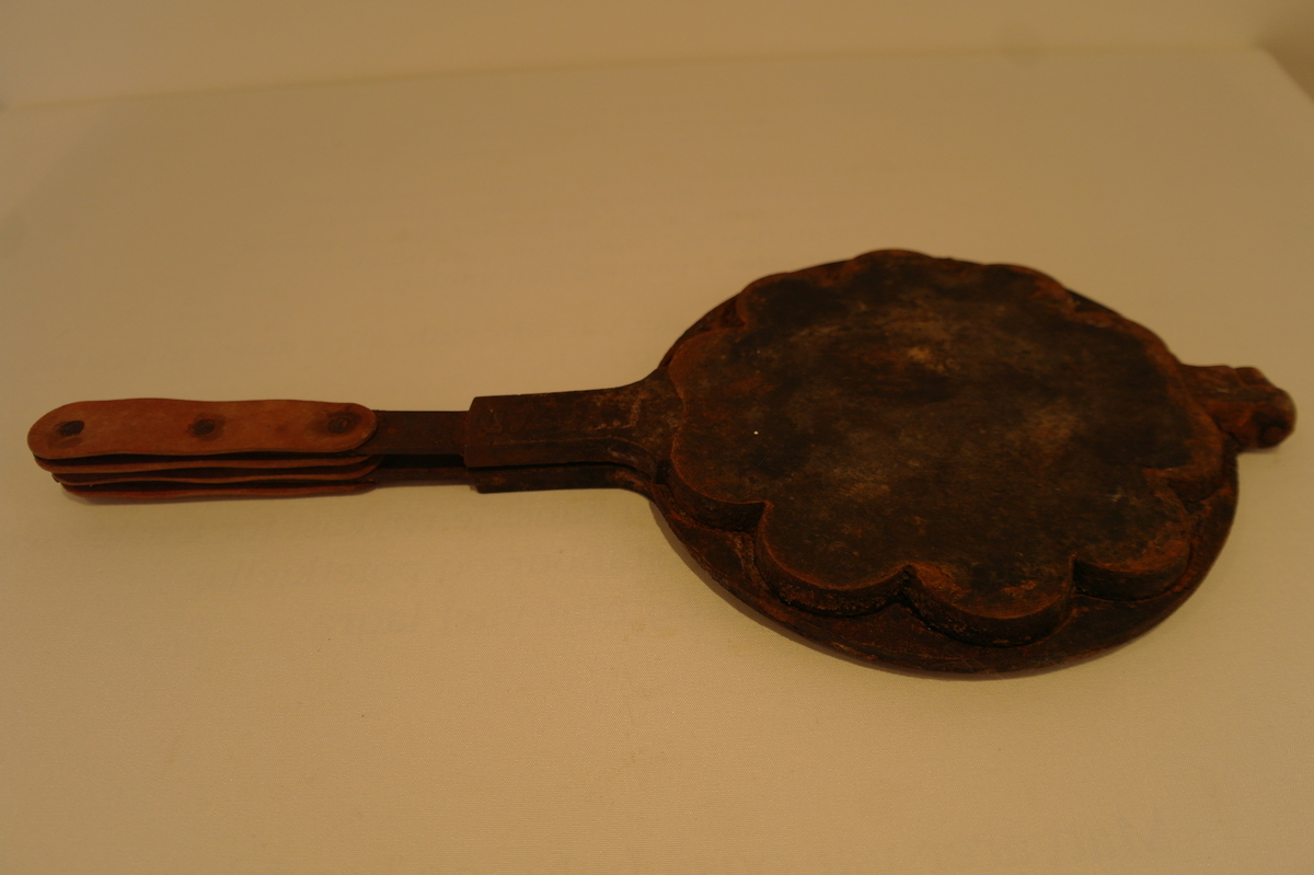 Vaffeljarn i jarn til bruk over vedovn. Produksjonsstempel:MUSTAD. På handtakene er det festa noko som liknar lær  med jarnnaglar. Innvendig er jarnet noko rusta.