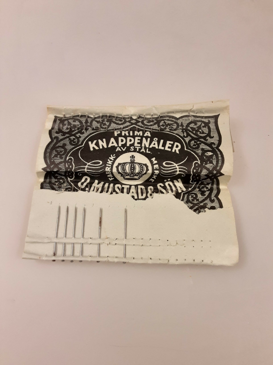 Papirbrett, grønt brett. 3 ufullstendige rekker med knappenåler, avrevet ark. Tekst: Prima Knappenåler av stål /  O. Mustad & Søn, Oslo nr . 8