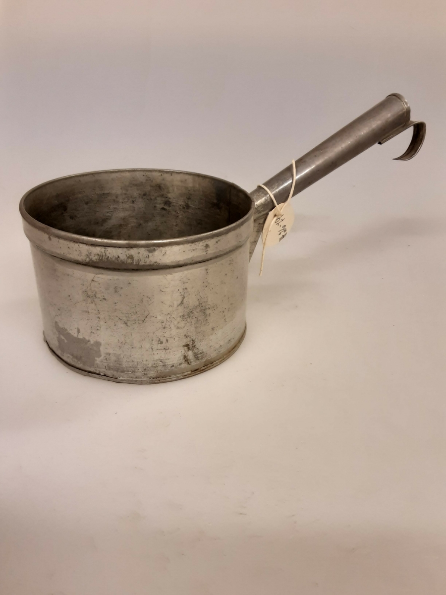 Blikk, falset og loddet. Ytterst på hanken er en krok for oppheng. Målet rommer 1 liter væske.
