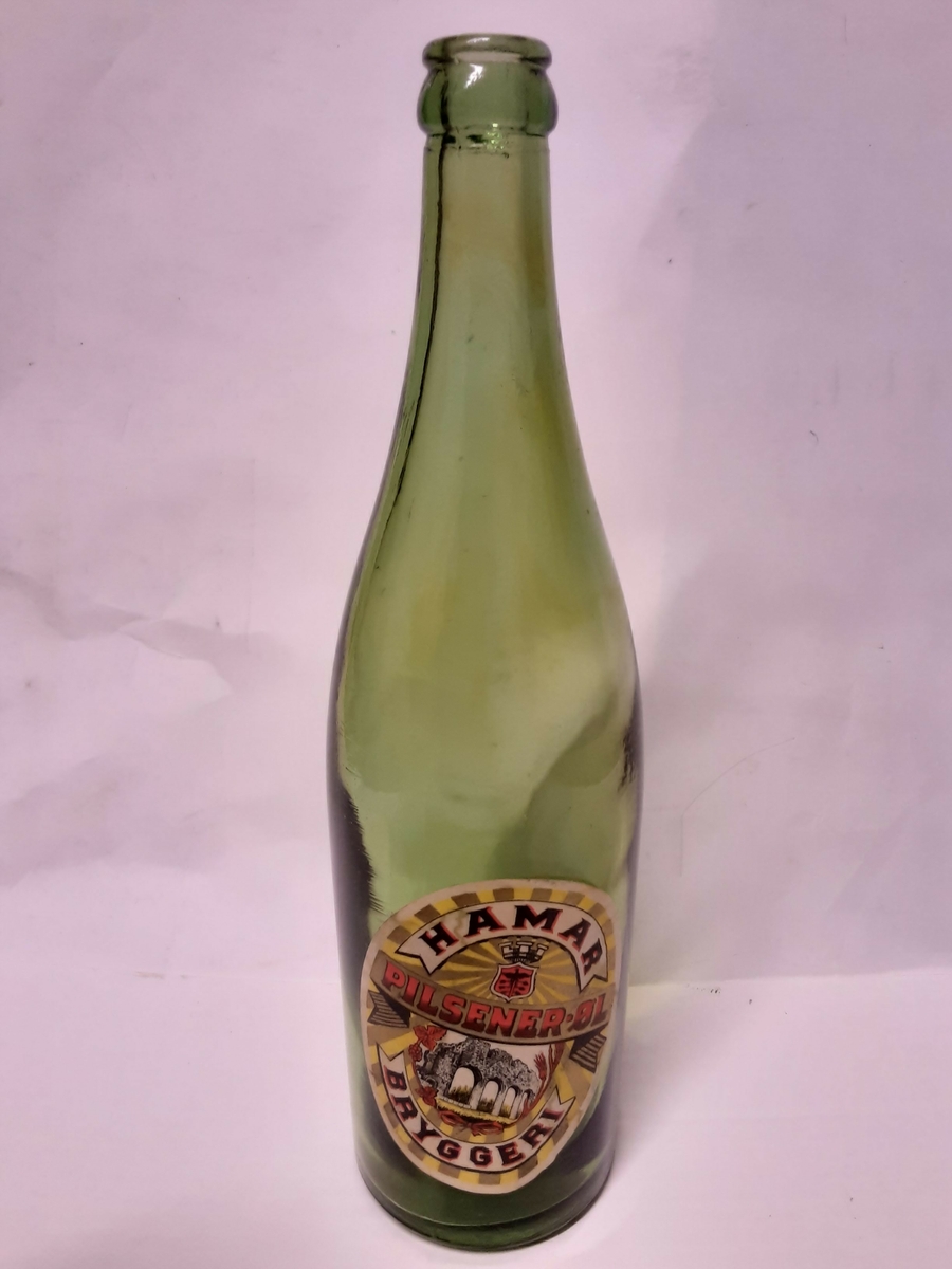 Grønt glass. Papiretikett, gul bunn, stråler i gull, bokstaver i rødt og sort, bilde av Domkirkeruinene og Harnar byvåpen.