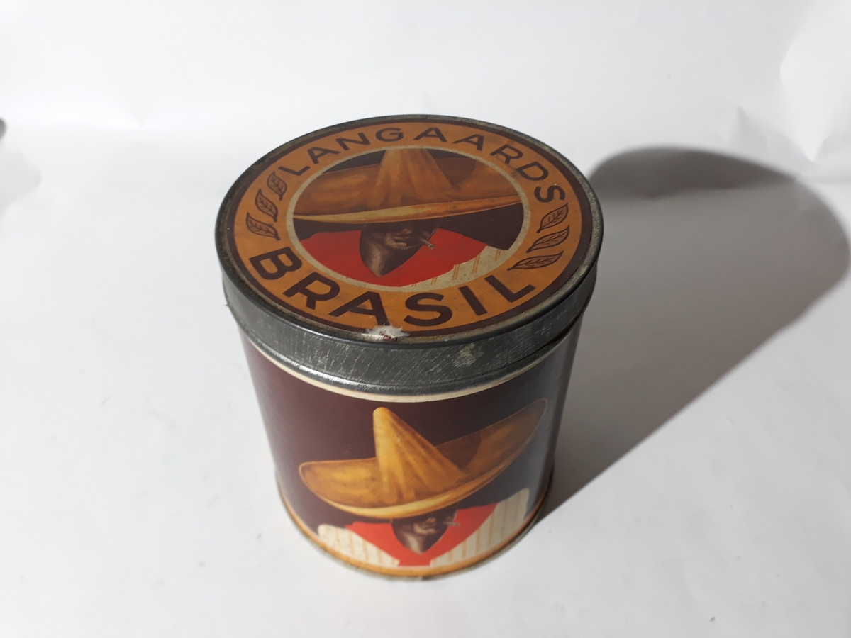 Blikk. Boks med lokk. Trukket med papir, brun bunn, lysebrune og hvite bokstaver. Etter stilpreg fra 1930 årene.