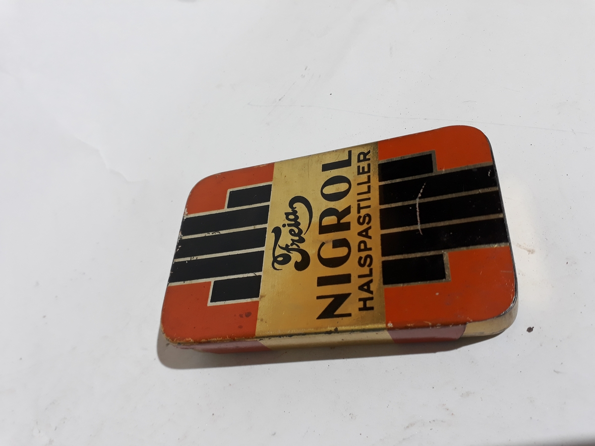 Metall. Rektangulær form med avrundede hjørner, med skyvelokk. Motiv i orange, sort, og gull. Etter stilpreg fra 1930 -40 årene.