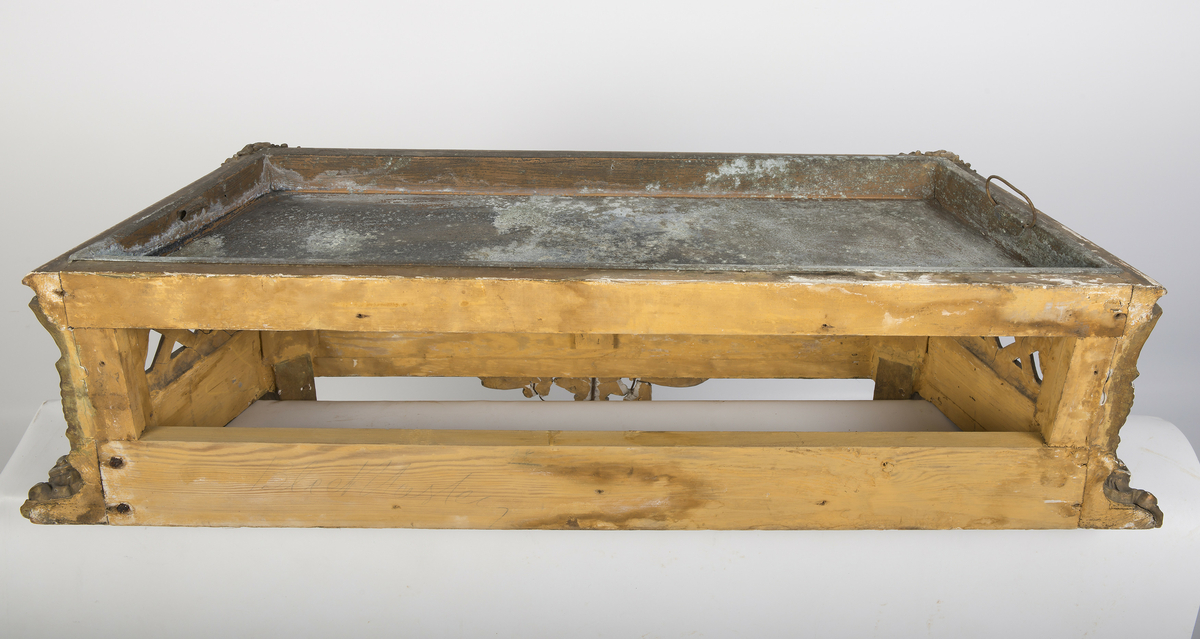 Lavt konsollbord med utskårne elementer; ett kvinnehode på hvert hjørne. Rik rokokkodekor som er forgyldt. Metallbakke nedfelt på toppen. Antagelig for blomsterdekorasjon.