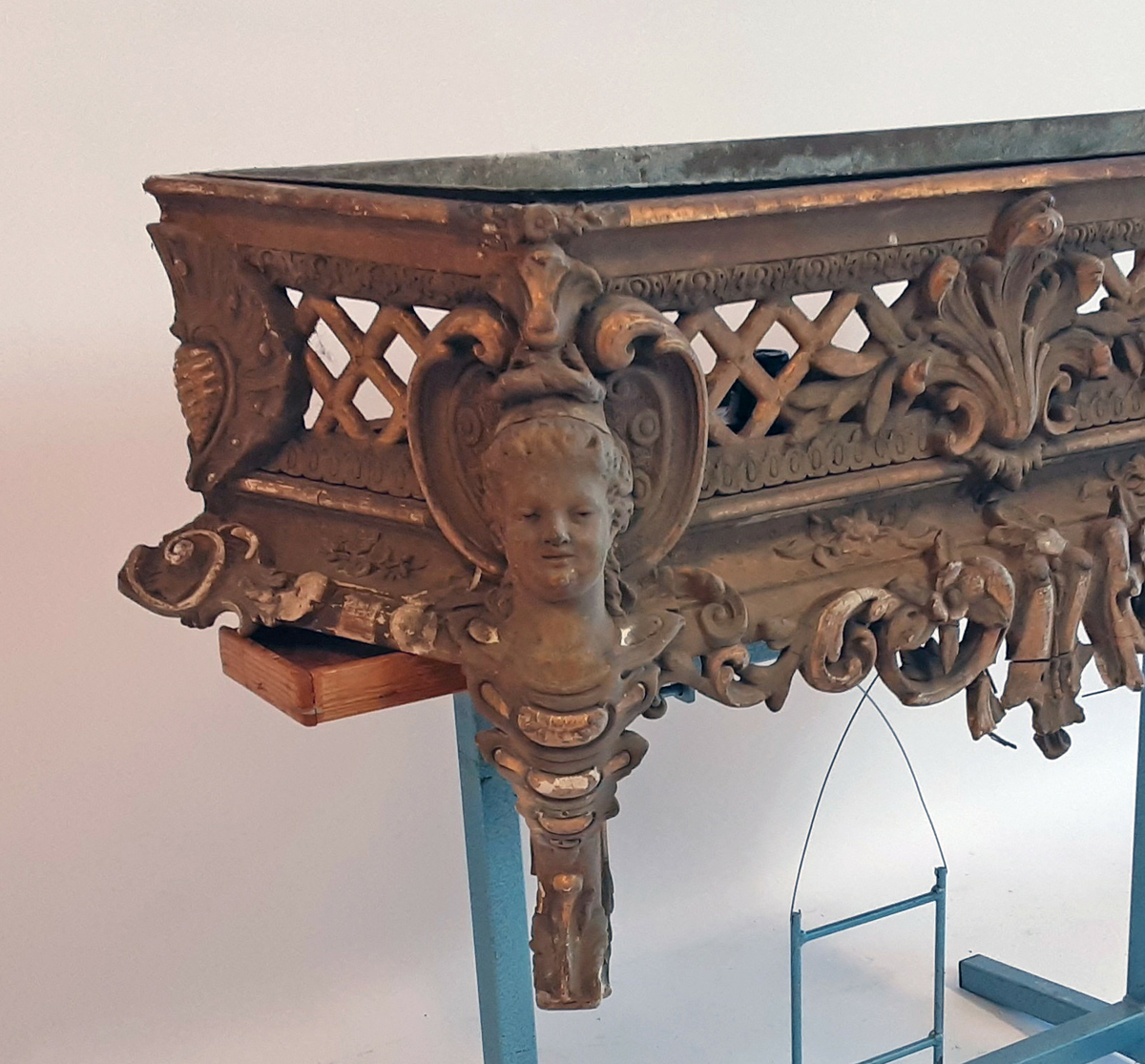 Lavt konsollbord med utskårne elementer; ett kvinnehode på hvert hjørne. Rik rokokkodekor som er forgyldt. Metallbakke nedfelt på toppen. Antagelig for blomsterdekorasjon.