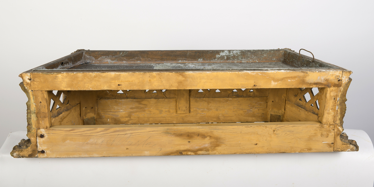 Lavt konsollbord med utskårne elementer; ett kvinnehode på hvert hjørne. Rik rokokkodekor som er forgyldt. Metallbakke nedfelt på toppen. Antagelig for blomsterdekorasjon.