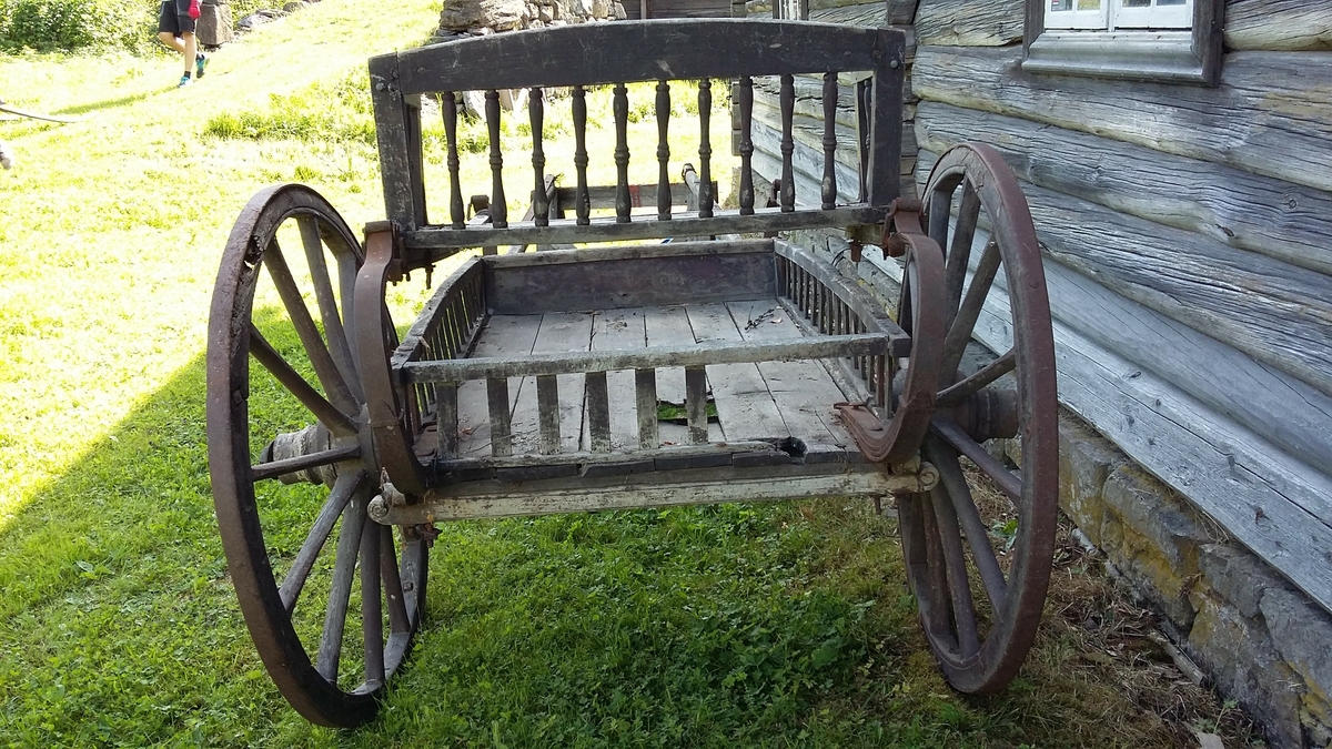 Vogn med to hjul, stol i c-fjærer foran og bak (sviktende trefjærer), ett tverrstilt sete (dreide spiler). Slett kassebunn med flate svakt s-formete spiler. 
Greaseaksel.
Jernbeslåtte hjul.
Antall trefell: 6
Antall eiker: 12
Det er rissa to tynne stafferingsstreker på hjulene og med vulst på innsida.