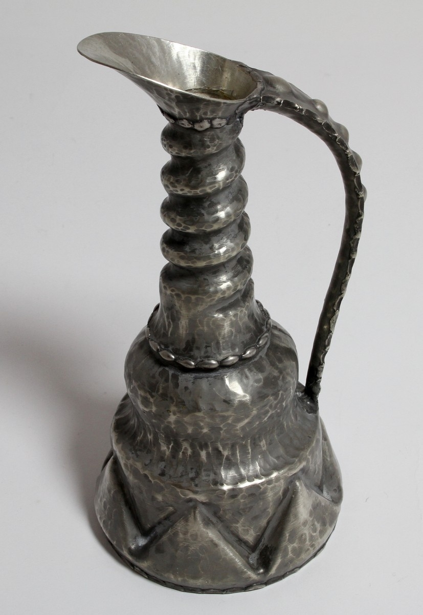 Tinnkanne frå tinnsamlinga til Hanna Rytter, som har stått på Rytterhaugen. Far til Hanna Rytter var diktaren Henrik Rytter (1877-1950). I gåvebrevet til Hol Folkebibliotek datert 1976, skriv ho: "Utanom dette er det ei lita gåve frå mi tinnsamling på "Rytterhaugen" som har hatt plassen sin i peisestova der sidan Henrik Rytter døde i 1950. Det er eit krus, ei kanne og 2 små drikkehorn som er handsmidde og kjem frå tinnsmed på Nesbyen."