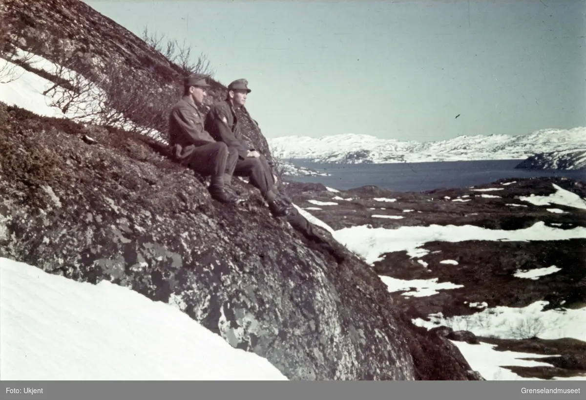 To soldater sitter i en fjellside og ser utover. Ved Kirkenes med utsikt ut over Reinøya og Hælen. 