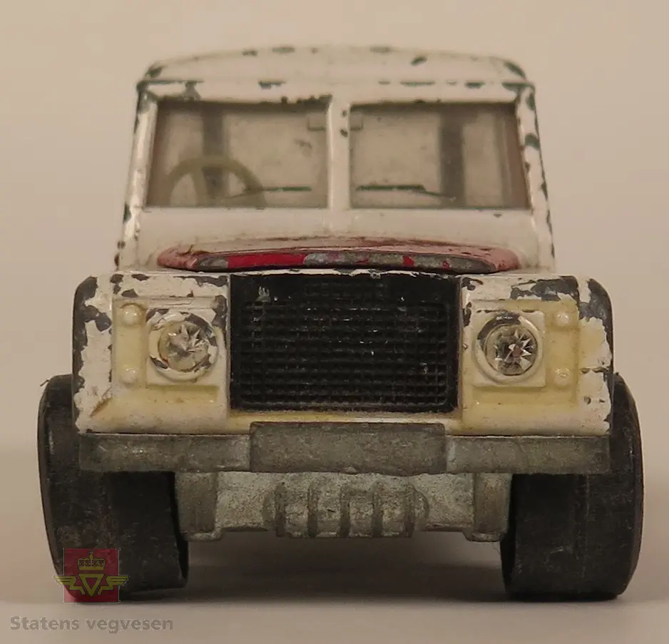 Hovedsakelig hvit og sekundært rød Land Rover modell. Den er laget av metall og mangler en kran på lasteplanet og varsellys på taket. Skala 1:43