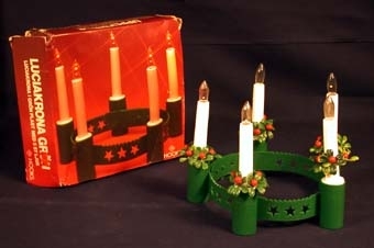 :1 Krans av ett 30 mm brett band av mörkgrön plast på några ställen dekorerad med stjärnor och hjärtan utskurna i plasten. Kransens omkrets kan ställas in i tre olika lägen beroende på hur stort det huvud som ska bära den är. På kransens utsida sitter fem stycken hållare för ljus. I dessa ska ett batteri placeras och ovanpå det 100 mm höga ljuset i plast med glödlampa på toppen som lyser med hjälp av batteriet. På insidan av kransen ett klistermärke med röd tryckt text: "OBS! Låt inte barnen stoppa ljuset i munnen! Avlägsna batteriet ut hållaren efter användning".
:2-6 Fem stycken små kransar av grönt och rött plast som ska föreställa lingonris med bär, vilka ska träs övre kronans ljus som ett dekoration.
:7 Kvadratisk kartong, 220 X 220 mm, i vilken luciakronan köptes i. Av papp, på utsidan ett fotografi av en lysande luciakrona mot en röd bakgrund. Med vit tryckt text står: "Luciakrona grön. Luciakrona i grön plast med 5 st ljus. Hooks. Upplysning: Luciakrona i grön plast med inställbart pannband. 5 st 10 cm höga släta vita ljus. Ljushållaren fungerar som batterihållare. Topplampa 1,4 v. Alla batterifabrikat passar. Kontaktfjädrarna skall löpa i ett av det två spåren som finns i batterihylsan. Lampan tänds genom att skruvas i och släcks genom att skruvas ut".