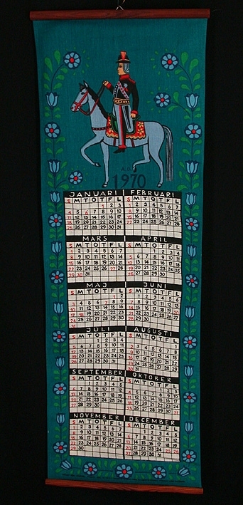 5 st väggalmanackor med färgtryck på linnetyg. 

:1 Almanacka från 1970. Brunbetsad trälist i över- och underkant. Själva almanackan i vitt, svart och rött. Ram och överstycke mörkt blågrönt med en slinga av blå blommor samt ett motiv med en ryttare till häst i folkloristisk stil. Längd 900 mm, bredd 305 mm.

:2 Almanacka från 1974. Brunbetsad trälist i över- och underkant. Oblekt linnetyg med tryck i orange, svart, grönt, gult och vitt . Själva almanackan omges på båda sidor av stjärntecken. Överstyckets motiv består av solen, månen, planeter och stjärnbilder. Längd 525 mm, bredd 330 mm. 

:3 Almanacka från 1985. Antikbetsad trälist i över- och underkant. Oblekt linne med tryck i brunt, rött, grönt, gult, blått och vitt. Själva almanackan utgör drygt halva längden, däröver 4 st motiv - ett för varje årstid. 
Längd 600 mm, bredd 320 mm.

:4 Almanacka från 1996. Obehandlad trälist i över- och underkant. Vitt, fintrådigt linne med tryck i grönt, rött, gult, blått och svart. Själva almanackan omges av bilder och namn på Sveriges landskapsblommor. 
Längd 710 mm, bredd 330 mm.

:5 Almanacka från 2000. Rund obehandlad pinne trädd i sydd kanal i tygets överkant. Vitt fintrådigt linne med tryck i blått, svart, rött, gult, grönt, brunt, rosa och grått. Själva almanackan utgör den nedre halvan av tyget. På den övre halvan avbildas en prislista med priser från år 1900 och år 2000. På båda sidor härom avbildas olika matprodukter och husgeråd. 
Längd 580 mm, bredd 350 mm.