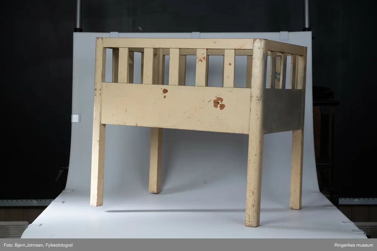 Gulmalt babyseng i tre. Tallet 2 er malt med svart på den ene kortsiden. Nederste del av senga er tett, øverste del har spiler, tre i hver kortside og fem i hver langside.