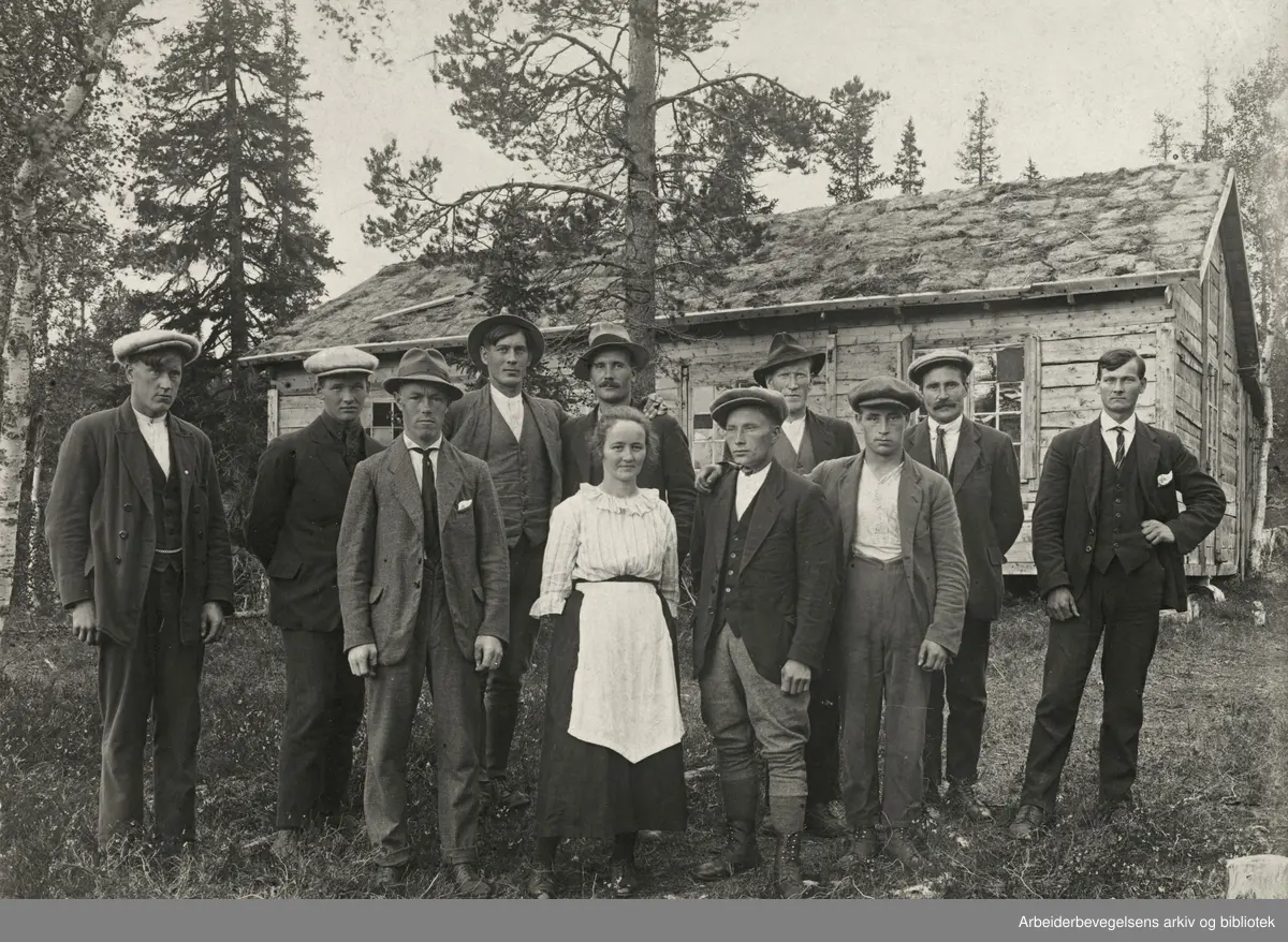 Anleggsarbeidere ved veianlegget (riksveien) på Namsskogan, ca. 1921. I bakgrunnen "storbrakka", der det lå to i hver seng. Kokke Inga Jensen, senere g.m. Ole Stubbforsmo. De øvrige på bildet er (f.v.) Leif Stubbforsmo, Undvig Kroken, Sverre Nilsen, Helge Fagerli, Petter Stubbforsmo, Ole Bergli, Ole Stubbforsmo, Lars Stormli, ukj. og Eldar Johansen.