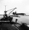 Flygplan S 5A, Heinkel He 5 Hansa lyfts upp på fartyg med lyftkran. Flygvapenpersonal och personal från marinen står på fartyget. 1930-tal.