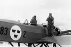 Militäre flygaren Verner Tornberg står i flygardräkt på vingen till flygplan S 5C Heinkel He 5 Hansa och förbereder sig för flygning. En man står på andra vingen. 1930-tal.