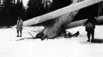 Ett havererat flygplan S 6 ligger med nosen i snö. Två män står vid flygplanet. 1930-tal.