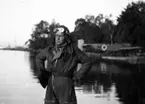 En man i flygarklädsel står vid vatten under övning i flygvapnet i juli-september 1935. I bakgrunden står flygplan S 5A målad med rödbruna cirklar över kronmärkena.