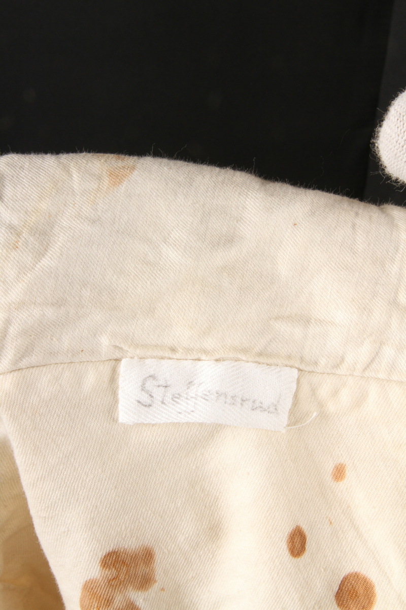 Enkeltknappet vest i lyst, mønstervevet bomullsstoff. , og uten krage. Den har seks håndsydde knapphull og like mange håndsydde småhull til spesialknapper. Samt to stikklommer og én brystlomme. Spensel, men ingen spenne, i ryggen. Vesten har et innvevd motiv som viser velosiped  med mann (Velte-Petter).