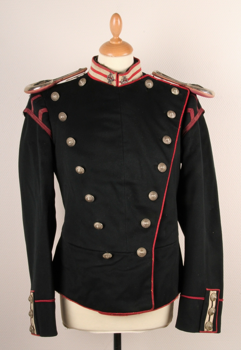 Offiserjakke fra den Norske Hæren. Svart jakke med røde og hvite dekorstriper under epaulettene. Stripene forestiller "svalereder" og lyrer på halskragen. Dette tyder på at jakka er uniform for en militær musiker. 14 sølvfargende knapper foran (to rader med 7 knapper) og 3 knapper på hvert erme. Knappene har diam: 23 mm. Jakka er norskprodusert.
Epaulettene på bilde 1 tilhører uniformen - er registrert som TM-12259