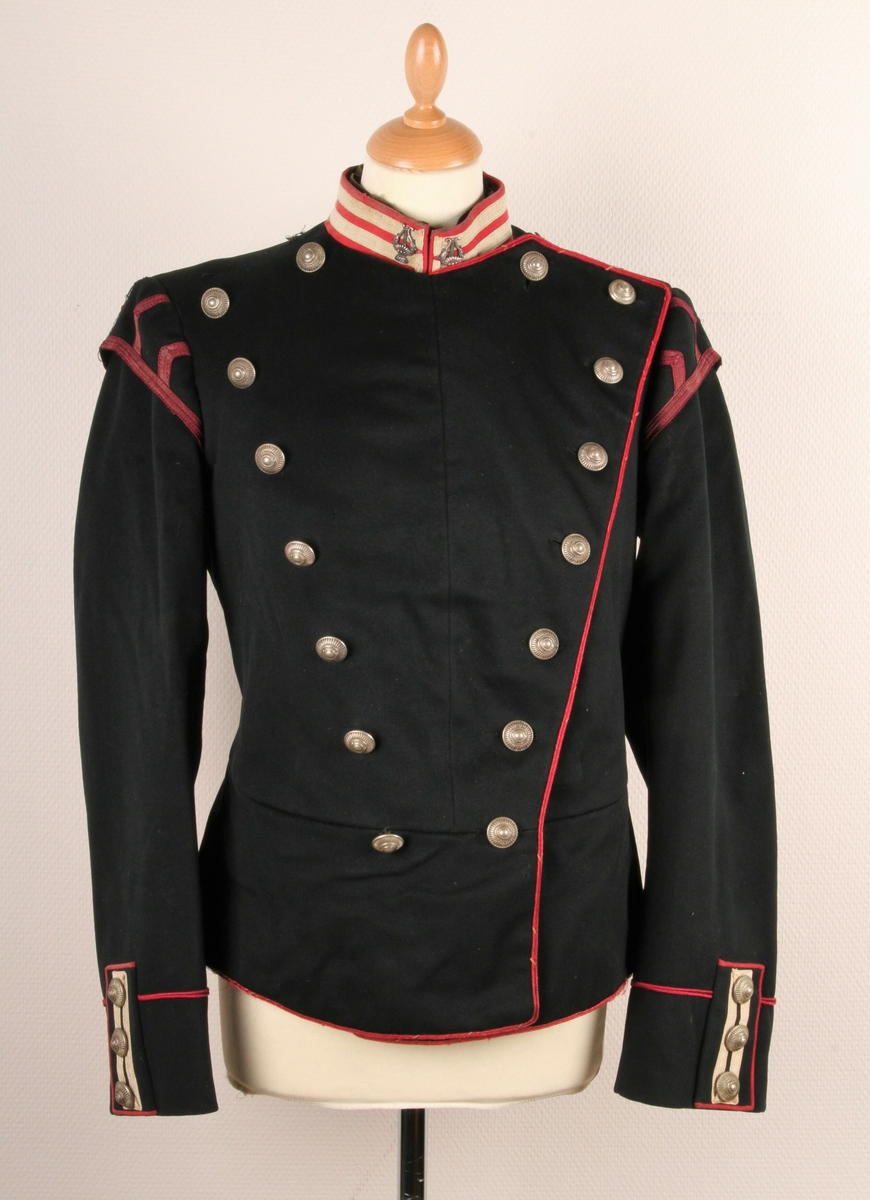 Offiserjakke fra den Norske Hæren. Svart jakke med røde og hvite dekorstriper under epaulettene. Stripene forestiller "svalereder" og lyrer på halskragen. Dette tyder på at jakka er uniform for en militær musiker. 14 sølvfargende knapper foran (to rader med 7 knapper) og 3 knapper på hvert erme. Knappene har diam: 23 mm. Jakka er norskprodusert.
Epaulettene på bilde 1 tilhører uniformen - er registrert som TM-12259