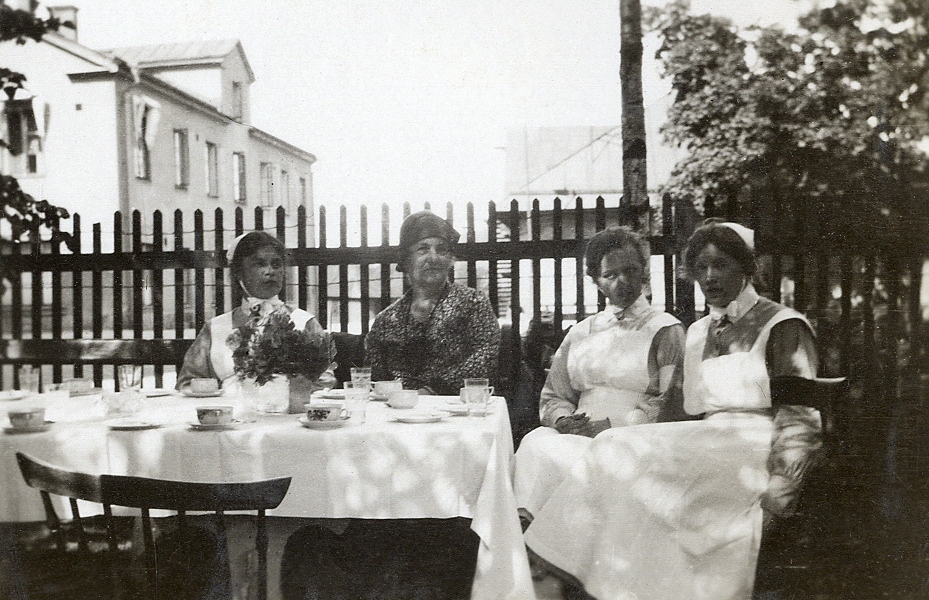 Några sjuksköterskor sitter tillsammans med en kvinna i hatt och kappa vid ett kaffebord utomhus. 
Text under fotot: "Martha-dagen, 1930".