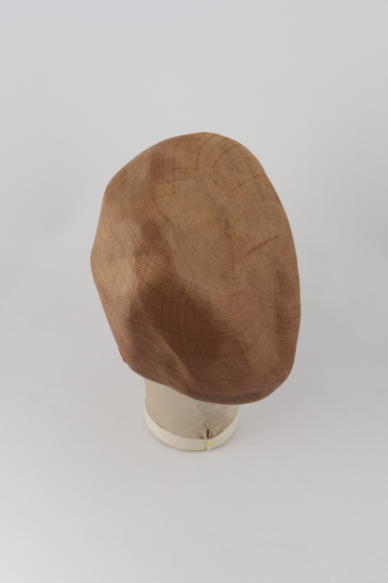 Brun hatt med brettet brem forann og påsydd remse med tvinnet tekstil ved bretten.