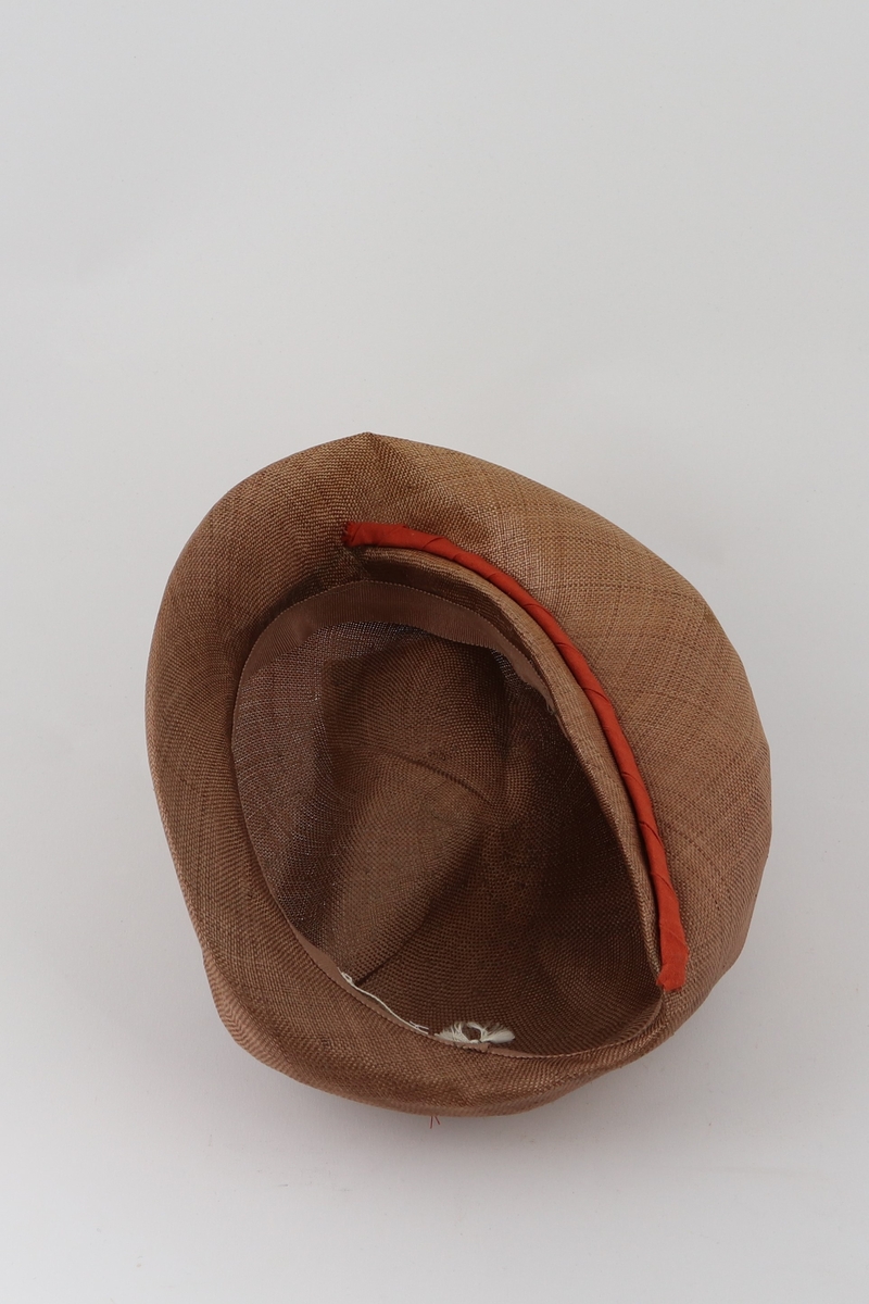 Brun hatt med brettet brem forann og påsydd remse med tvinnet tekstil ved bretten.