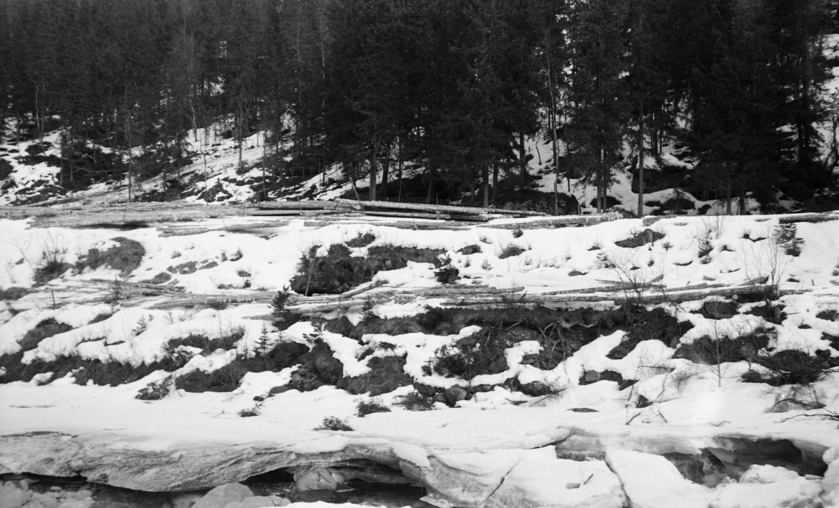 Tømmertillegging på snøen langs elva Vinstra i Nord-Fron kommune i Gudbrandsdalen. Stokkene ble lagt i små lunner med lengderetningen parallelt med strømretningen i elva, slik at det var enkelt å rulle dem ut i det rennende vannet når vannstanden høvde for fløting. Dette fotografiet ble tatt våren 1954.