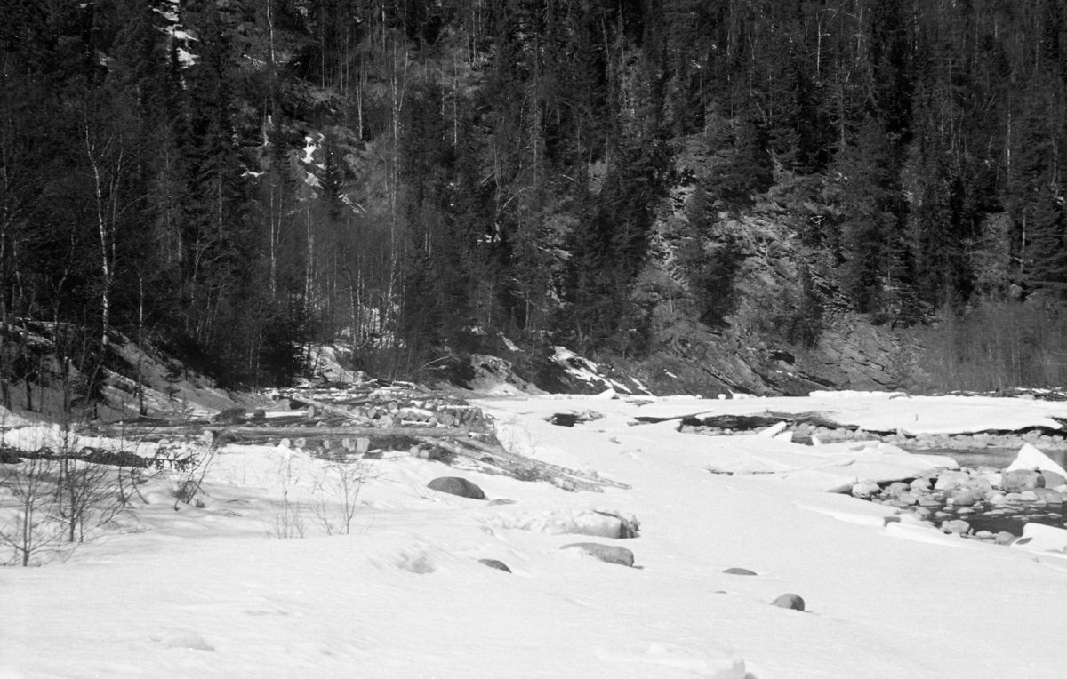 Tømmertillegging på snøen ved elva Vinstra i Nord-Fron kommune i Midt-Gudbrandsdalen, muligens i nærheten av Bjønnberget i Skåbu. Fotografiet ble tatt tidlig på våren i 1954, mens det ennå lå snø og is på og omkring elveløpet. Tømmeret var i hovedsak lagt i lunner der stokkenes lengderetning var parallell med strømretningen i elva, slik at det skulle være enkelt å rulle dem ut i det strømmende vannet når vårflommen kom.