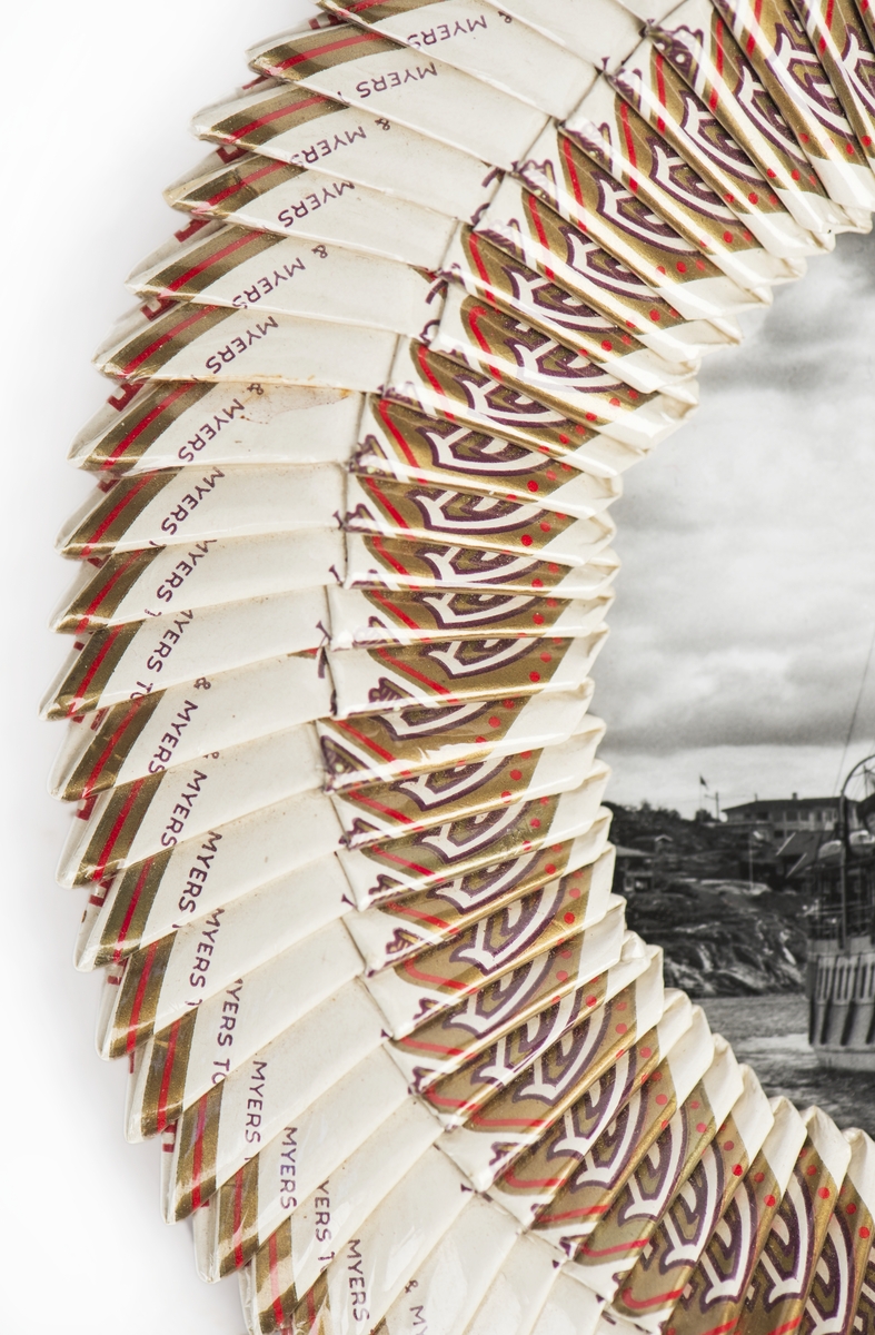 Inramat s/v fotografi av Ångaren "Bohuslän”.
Den runda ramen utgörs av vikta cigarettpaket.