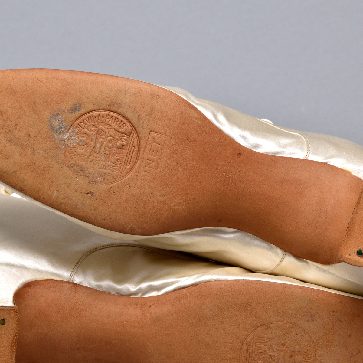 Ett par brudkängor av vitt siden tillhörande bruddräkt. Klädd insvängd klack, ca. 3 cm hög. Knäppning med 9 sidenklädda knappar och knapphål längs vågskuren kant på skons utsida. Skaftet med böljande kant. Mitt fram rosett av sidenband. Vitt foder av siden. Lädersula stämplad: PINET, Paris.