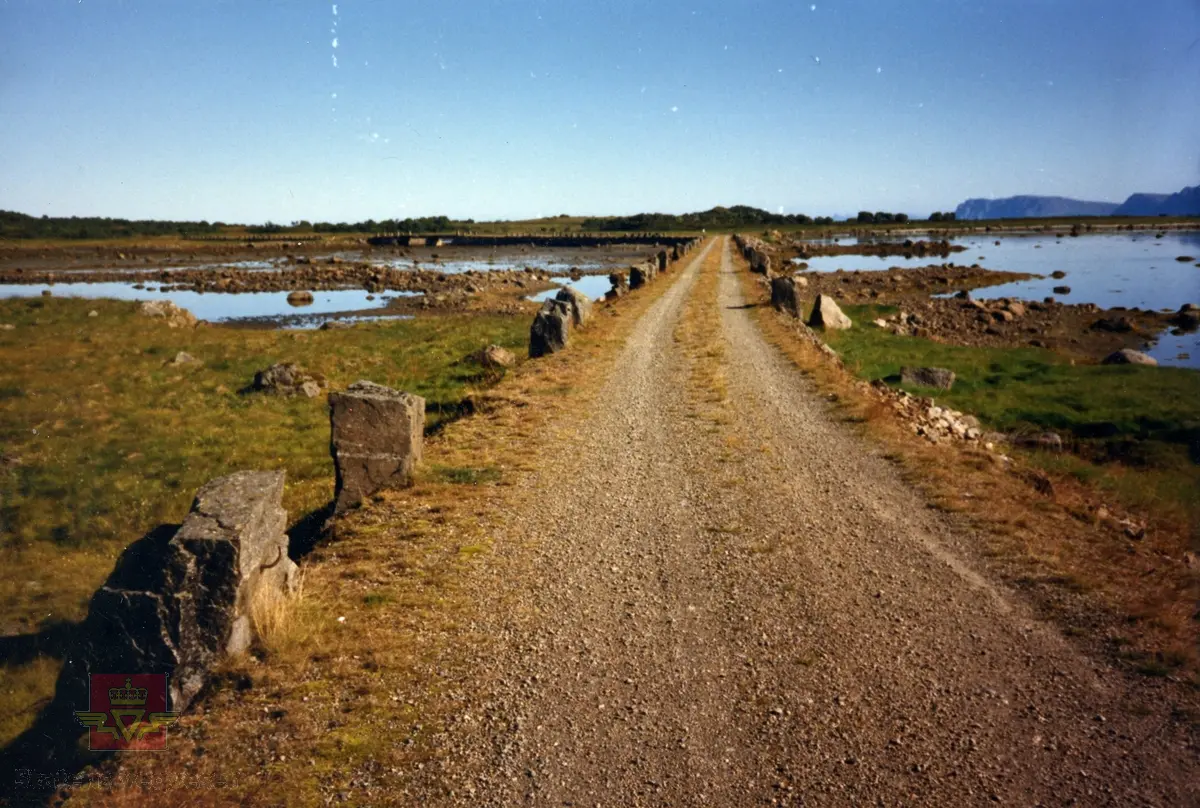 Bilde 1)  Kjøreveg fra 1922-1934. Fv.935. Strengelvåg fyllinga. 
Bilde 2) Refererer til bilde og informasjon Nr. 119 "Anlegget" Øksnes, Nordland, jf. Nasjonal verneplan, for veger, bruer og vegrelaterte kulturminner. Statens vegvesen - Region nord.  2002. 
Vegen ligger på en murt fylling i en lengde av 700 meter. På begge sider står stabbesteiner, og på midten av strekningen ligger ei nybygd stålbjelkebru på 24 meter over to spenn. Den er gjenoppbygd etter gamle tegninger og lagt på de opprinnelige brubjelkene. Brua har i dag innsnevring for å hindre motorisert ferdsel, men er i aktiv bruk som turveg.