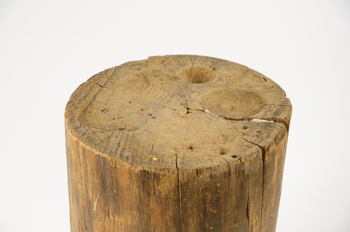 Hög stubbe med skålformade urgröpningar på ovansidan. Kraftig spricka e.torkning längst sidan, i sprickan är en bit vitt tyg instoppat . Stubben har många små sprickor och hål, vissa håligheter har fyllts igen med skumgummiliknande material. Rester av metall samt spikar finns i träet.