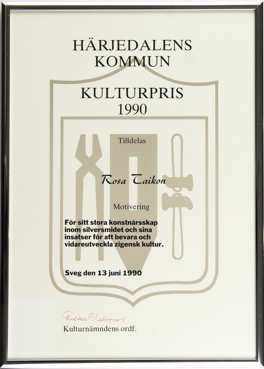 Diplom för Kulturpris från Härjedalens kommun till Rosa Taikon. Diplomet är av vitt papper med kommunvapnet tryckt i grått i bakgrunden. Texten är i svart och diplomet är inramat i en metallisk ram. I det nedre vänstra hörnet sitter en kort med blomdekoration.