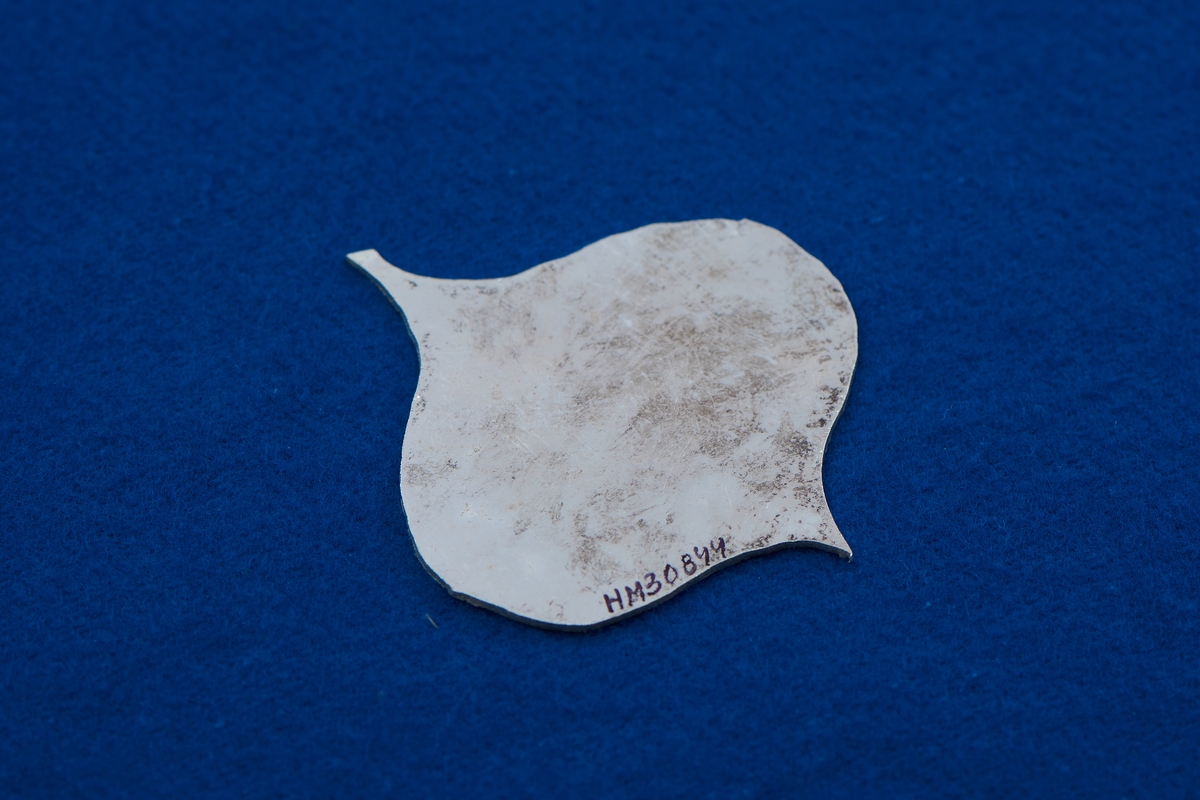 Silverplåt i spaderform med papper pålimmat på ena sidan. Den andra sidan lätt oxiderad.