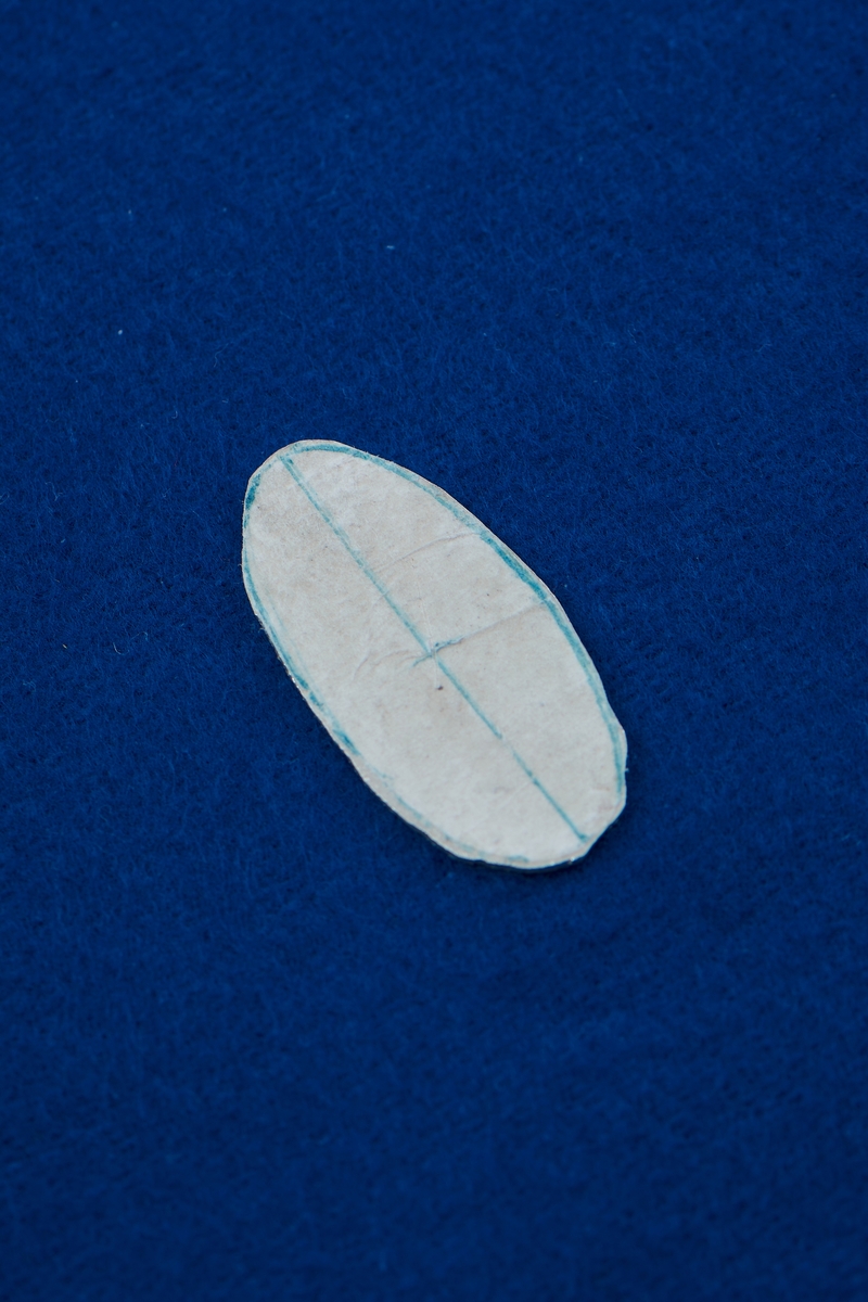 Silverplåt i oval form. På ena sidan finns papper fastlimmat. På pappret är streck ritade.  På andra sidan finns rester från avslitet papper.