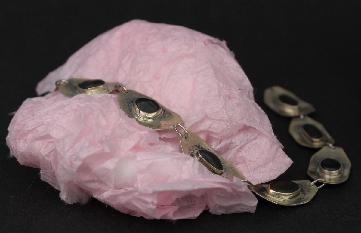 Armband i silver med svarta cabochonslipade stenar i sargfattningar. Armbandet består av åtta konkava silverbitar sammanlänkade av bindöglor. 
Armbandet är ett av Rosa Taikons första silversmycken, tillverkat 1961 vid en kvällskurs på Kursverksamheten i Stockholm. Efter kursens slut tog Taikon med sig armbandet till rektorn på Konstfacksskolan. Hon visade sina verk och berättade om sin bakgrund. Trots att Taikon saknade utbildning blev hon antagen som specialelev på Konstfack. Hon gick först två år på den Konstindustriella dagskolan, därefter tre år på Högre konstindustriella skolan.