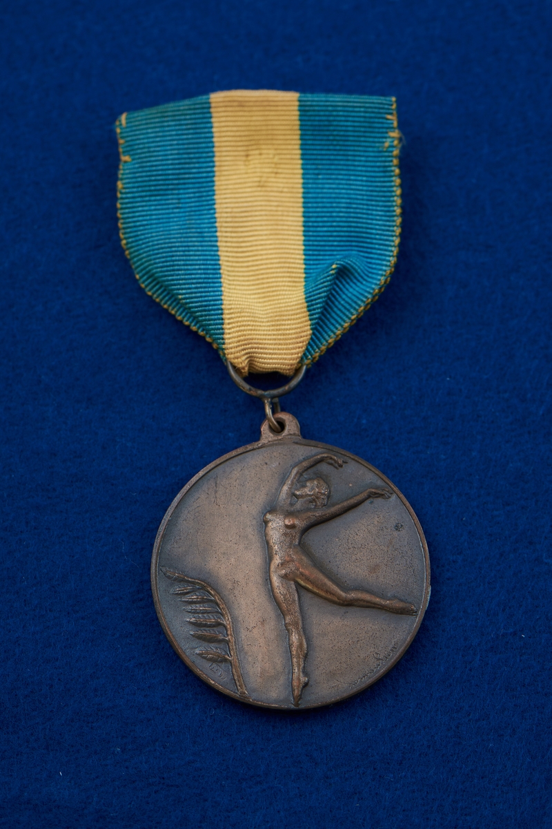 Medalj i brons fäst på blågult band. Medaljen har rund form med en naken kvinna i relief på framsidan.