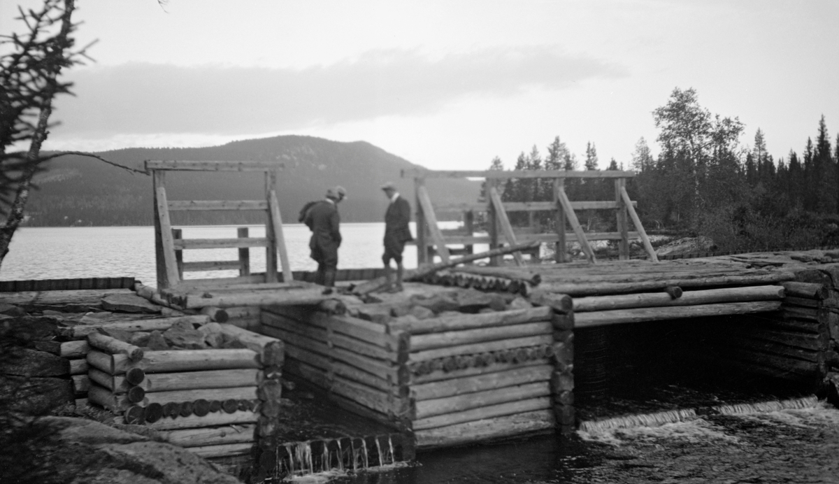 Lukedam av tømmer og stein. To personer. Dam ved Skjerva, Lunner, Oppland.