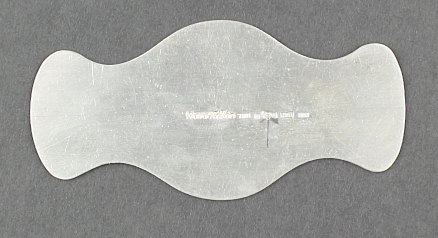 En silverplåt i geometrisk form. Plåten är ett stycke som ska bockas till ett armband. Plåten har svängda och rundade former.