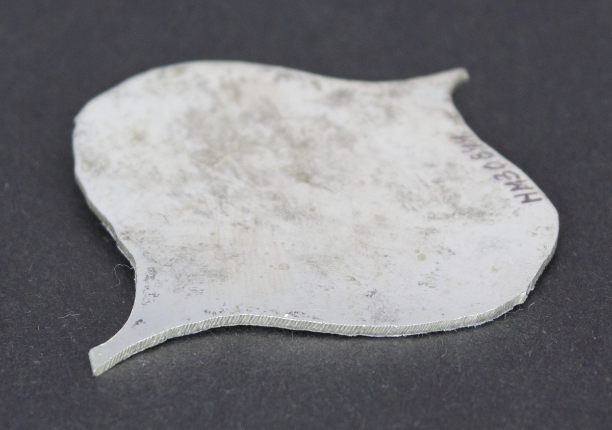 Silverplåt i spaderform med papper pålimmat på ena sidan. Den andra sidan lätt oxiderad.