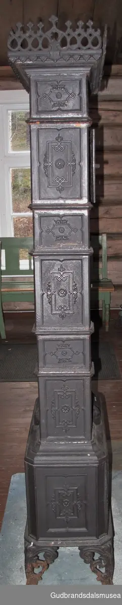 Etasjeovn med tre etasjer. Stiltrekk fra historismen på slutten av 1800-tallet. Brennkammeret har avskårne hjørner, er smalt, rektangulært med ilegging fra kortenden, enkel kokeplate med ringer på toppen samt askebakke foran døren. Står på fire bein av støpejern, bukkeføtter med bruskformer. Etasjekamrene har små dører med smijernsdekor.