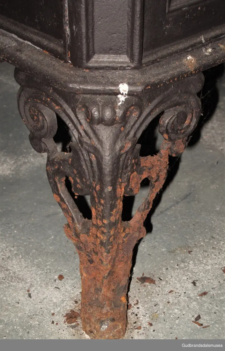 Etasjeovn med tre etasjer. Stiltrekk fra historismen på slutten av 1800-tallet. Brennkammeret har avskårne hjørner, er smalt, rektangulært med ilegging fra kortenden, enkel kokeplate med ringer på toppen samt askebakke foran døren. Står på fire bein av støpejern, bukkeføtter med bruskformer. Etasjekamrene har små dører med smijernsdekor.