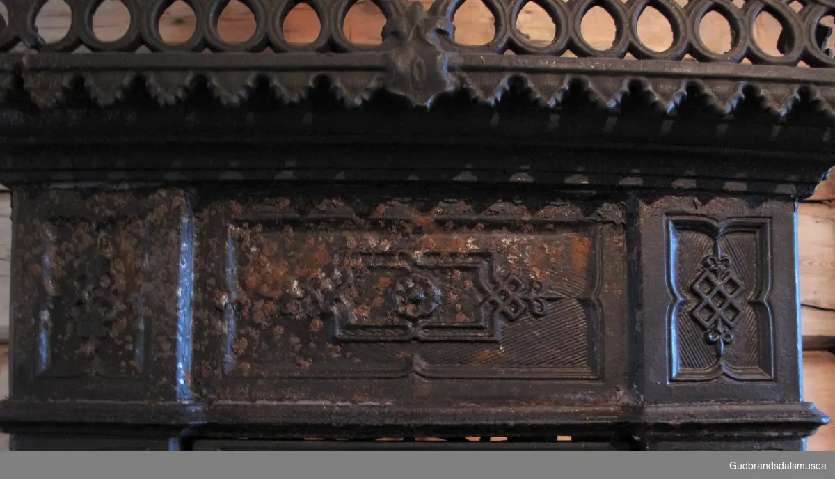 Etasjeovn med tre etasjer. Stiltrekk fra historismen på slutten av 1800-tallet. Brennkammeret har avskårne hjørner, er smalt, rektangulært med ilegging fra kortenden, enkel kokeplate med ringer på toppen samt askebakke foran døren. Står på fire bein av støpejern, bukkeføtter med bruskformer. Etasjekamrene har små dører med smijernsdekor.