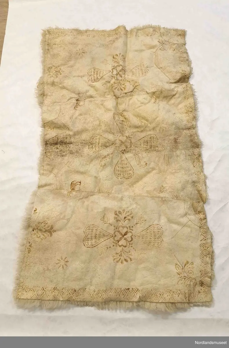 Rektangulær skinnfell laget av tre saueskinn sydd sammen. Fellen kan opprinnelig ha vært dobbelt så bred da den kun har kantbord i ene enden. Det er også rester av søm på den enden som mangler kantbord. 

Skinnfellen er dekorert med trykk av krinemønster. Her ser vi blant annet en hest.