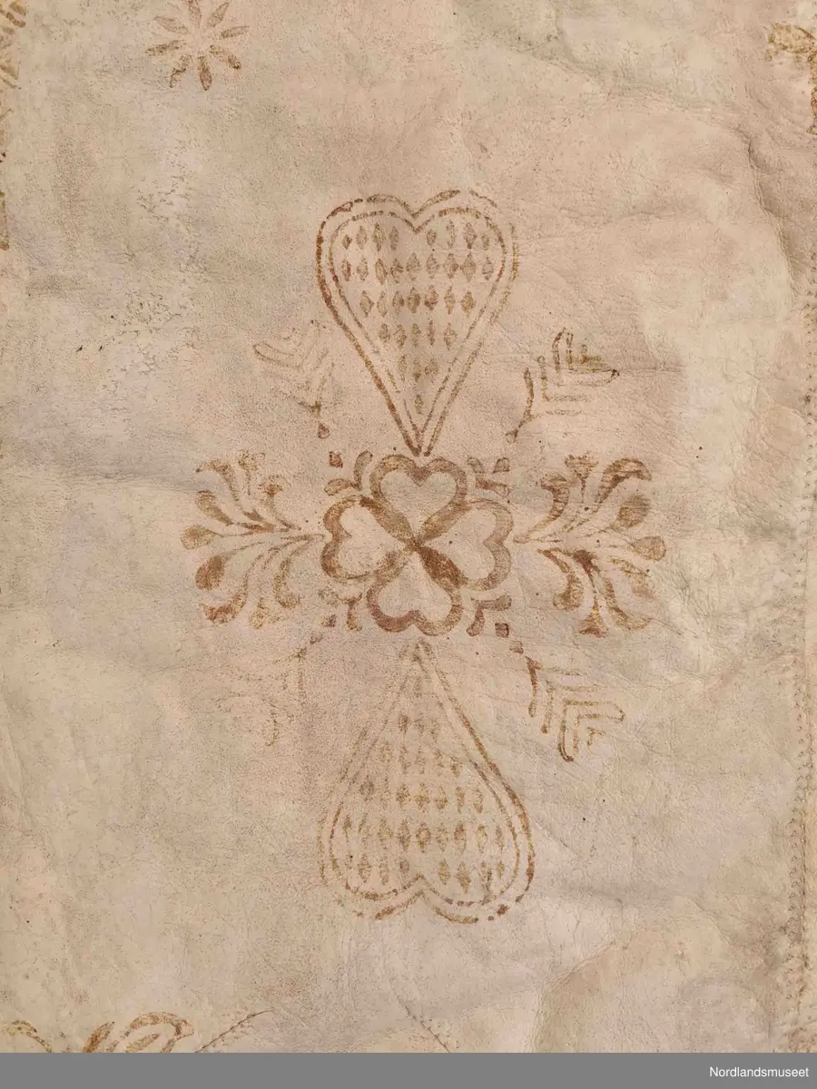 Rektangulær skinnfell laget av tre saueskinn sydd sammen. Fellen kan opprinnelig ha vært dobbelt så bred da den kun har kantbord i ene enden. Det er også rester av søm på den enden som mangler kantbord. 

Skinnfellen er dekorert med trykk av krinemønster. Her ser vi blant annet en hest.