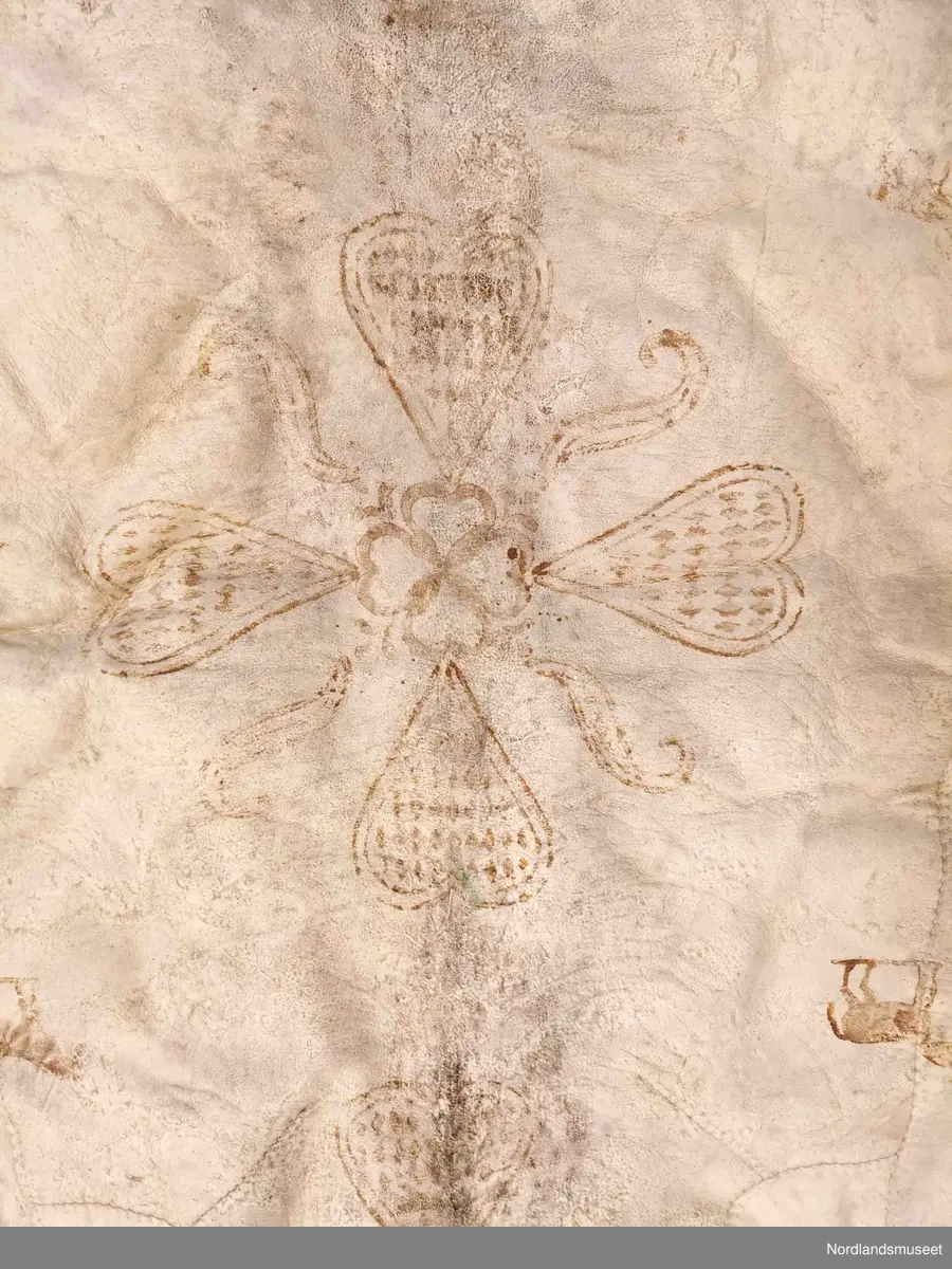 Rektangulær skinnfell laget av tre saueskinn sydd sammen. Fellen kan opprinnelig ha vært dobbelt så bred da den kun har kantbord i ene enden. Det er også rester av søm på den enden som mangler kantbord. 

Skinnfellen er dekorert med trykk av krinemønster. Her ser vi blant annet en hest.