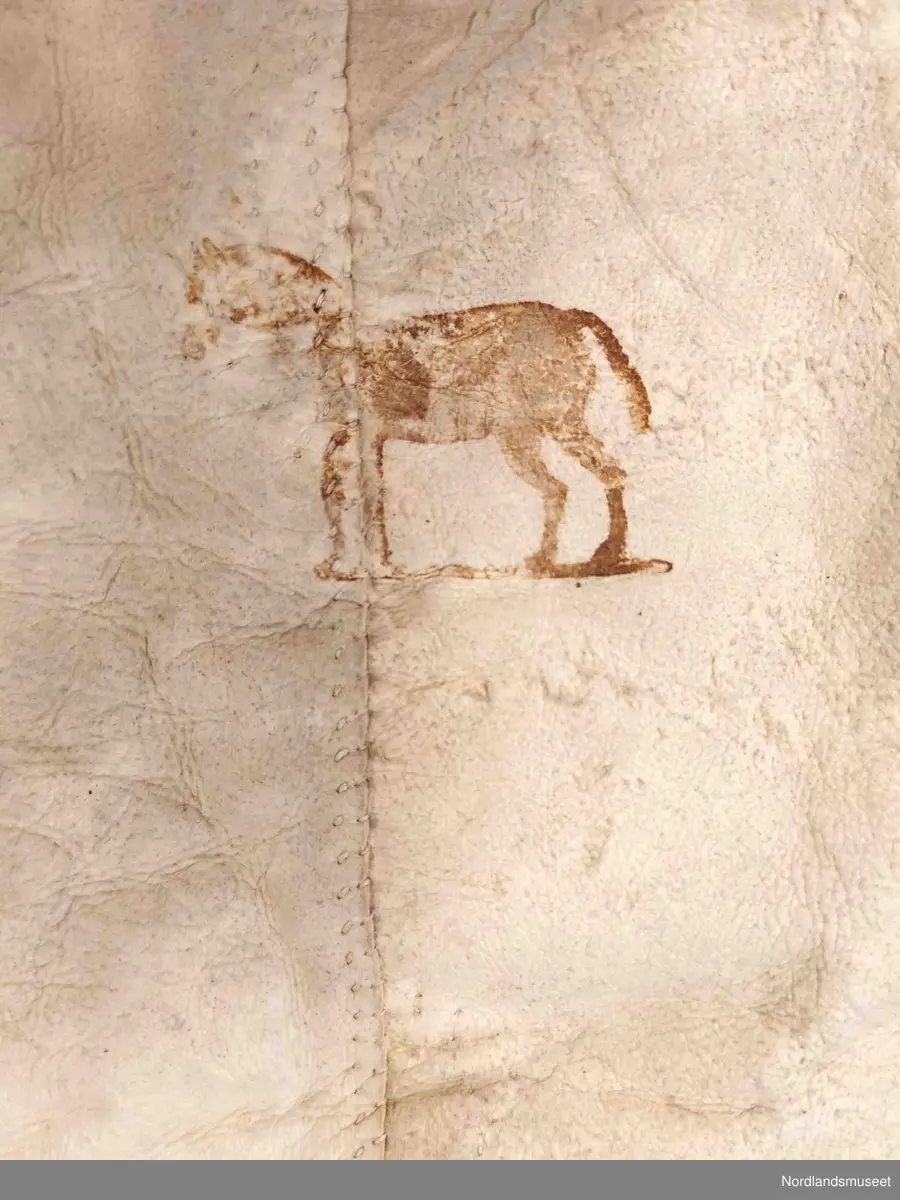 Rektangulær skinnfell laget av tre saueskinn sydd sammen. Fellen kan opprinnelig ha vært dobbelt så bred da den kun har kantbord i ene enden. Det er også rester av søm på den enden som mangler kantbord. 

Skinnfellen er dekorert med trykk av krinemønster. Her ser vi blant annet en hest.