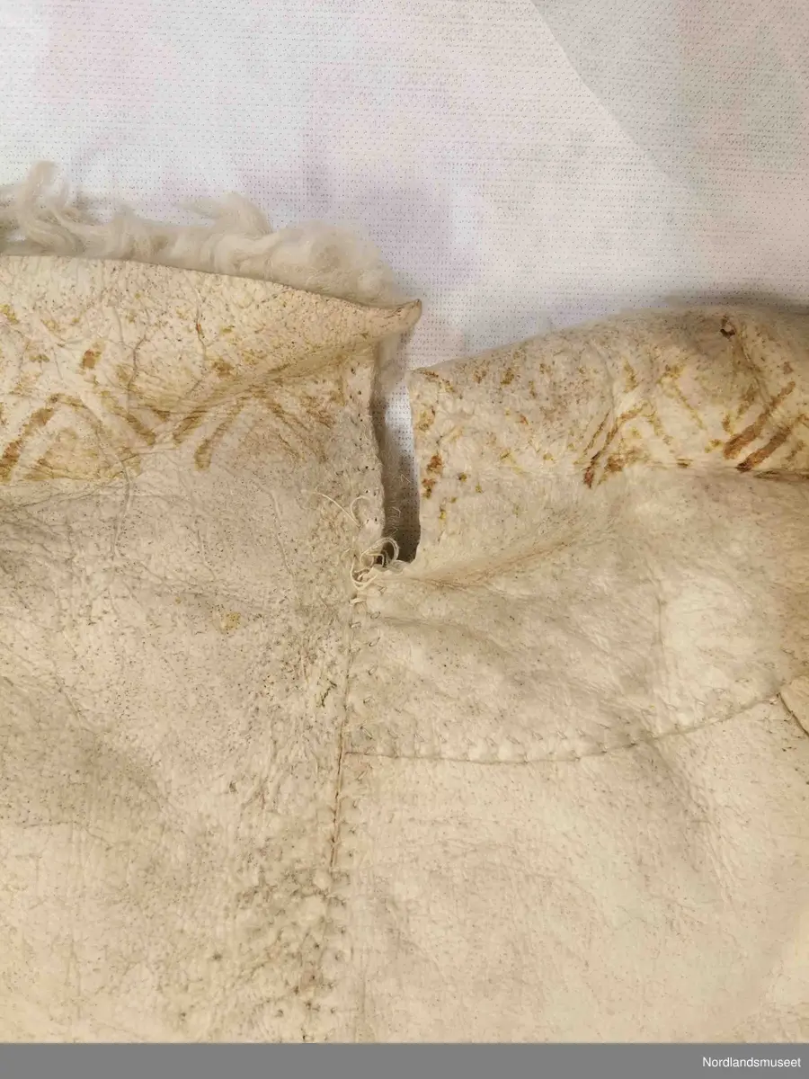 Rektangulær skinnfell laget av tre saueskinn sydd sammen. Fellen kan opprinnelig ha vært dobbelt så bred da den kun har kantbord i ene enden. Det er også rester av søm på den enden som mangler kantbord. 

Skinnfellen er dekorert med trykk av krinemønster. Her ser vi blant annet en hest.