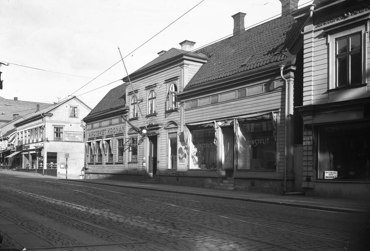 Västra Storgatan österut i Jönköping, vid korsningen med Barnarpsgatan. Där ligger bland annat Apoteket Kronan och Konstflit. På hörnet vid tvärgatan till höger finns en tobaksaffär och bredvid ligger S Berggrens hattaffär. På husets andra våning sitter en skylt, med texten "Krüger & Assarsson egendomsaffär, uthyrningsbyrå, obligationskontor". Även på fönstren där verksamhetens finns står delar av texten.